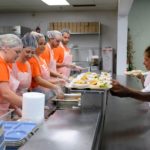 Volunteers serve food to clients in kitchen